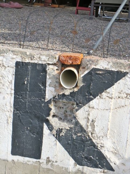 The original plan was to have the end of the tube drain out of the middle of the K.  Turns out that the cement there was over 6 inches thick.  The guys were done asn wanted to go home so they decided to move the end of the tube much higher up.